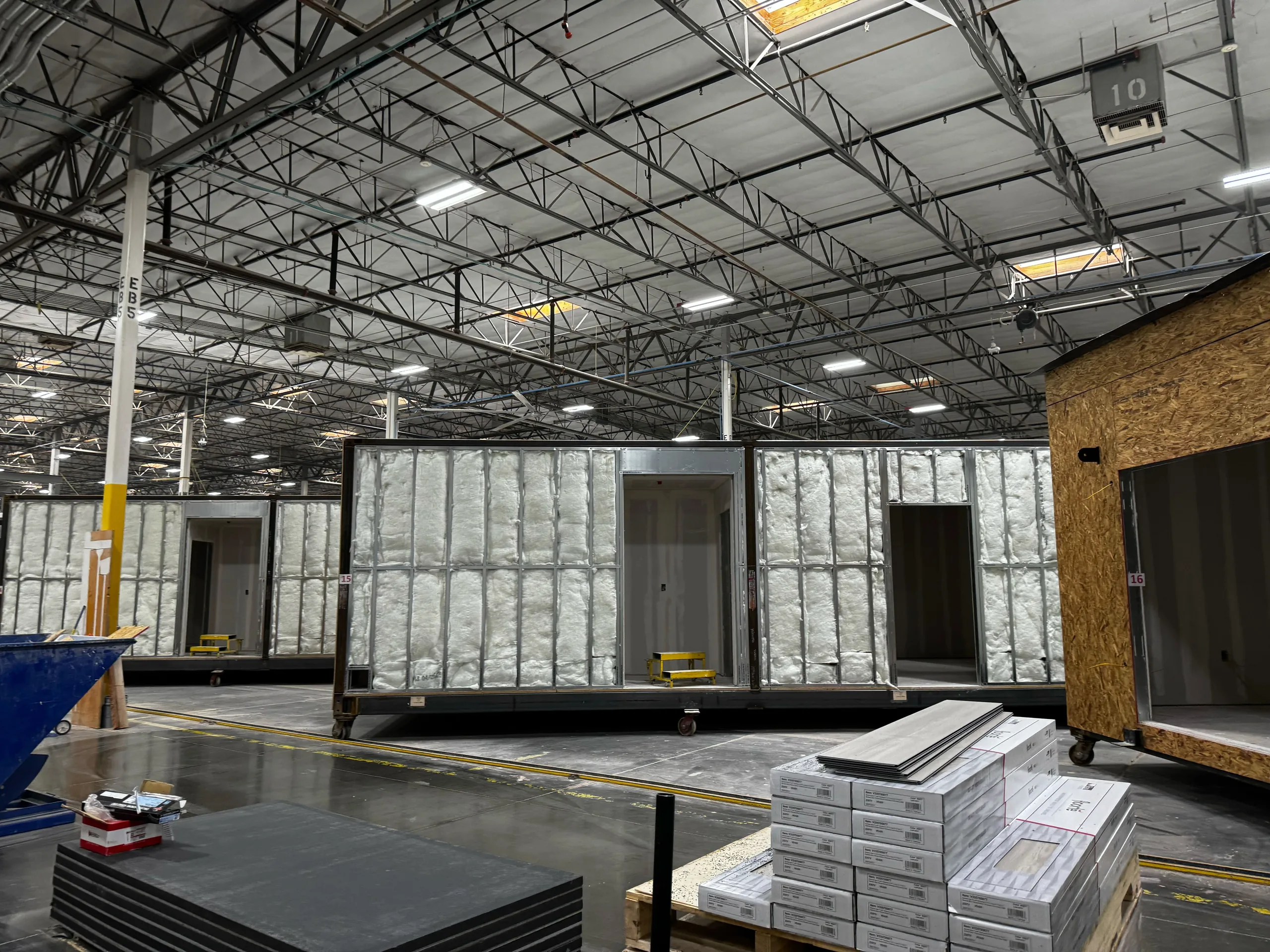 Steel-framed modules on carts down a plant bay, exterior walls open and insulated