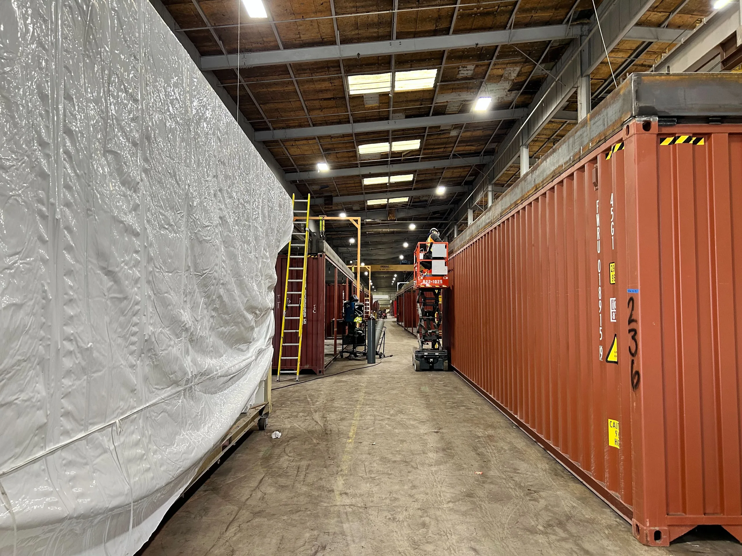 A shrink-wrapped module beside a row of shipping containers in the despatch aisle