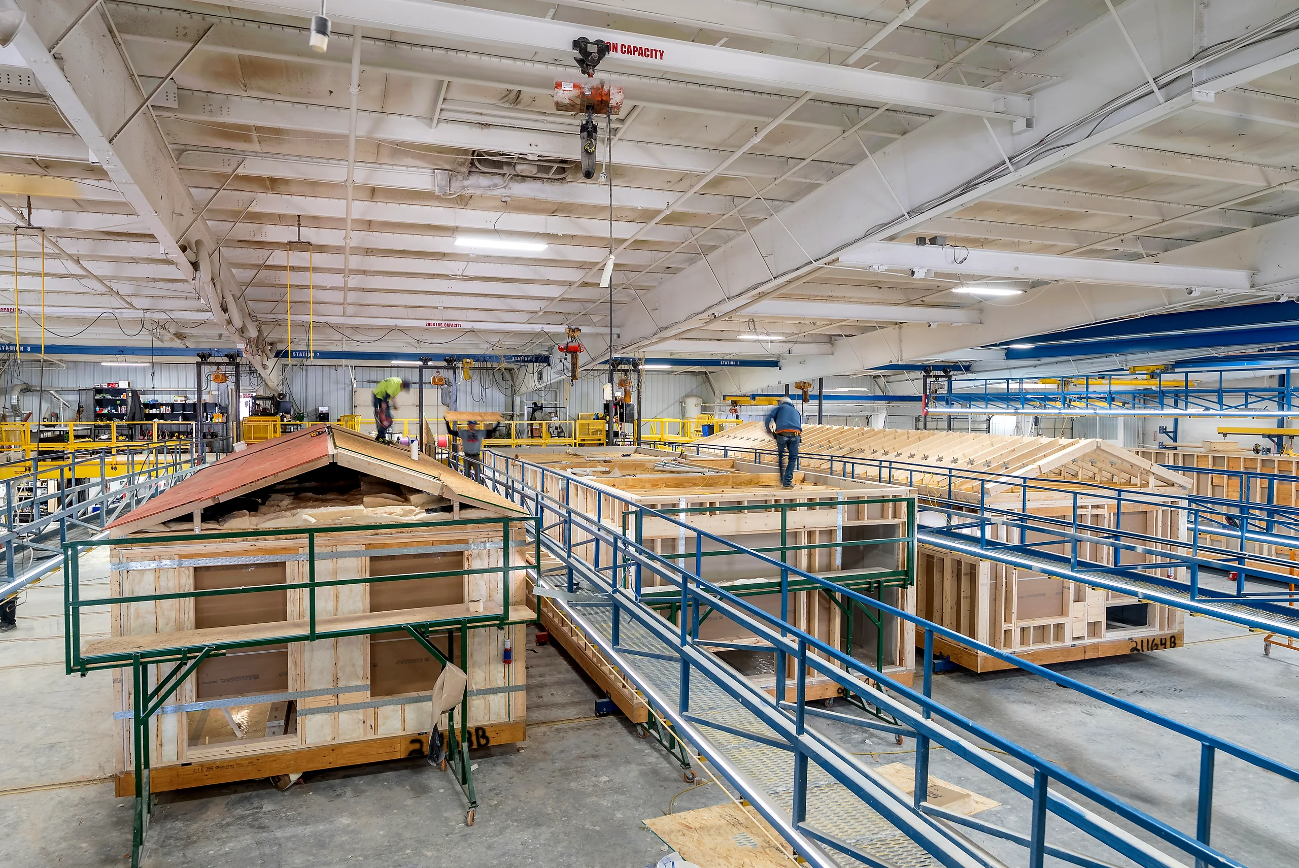 A prefabrication plant with completed modules moving under an overhead crane