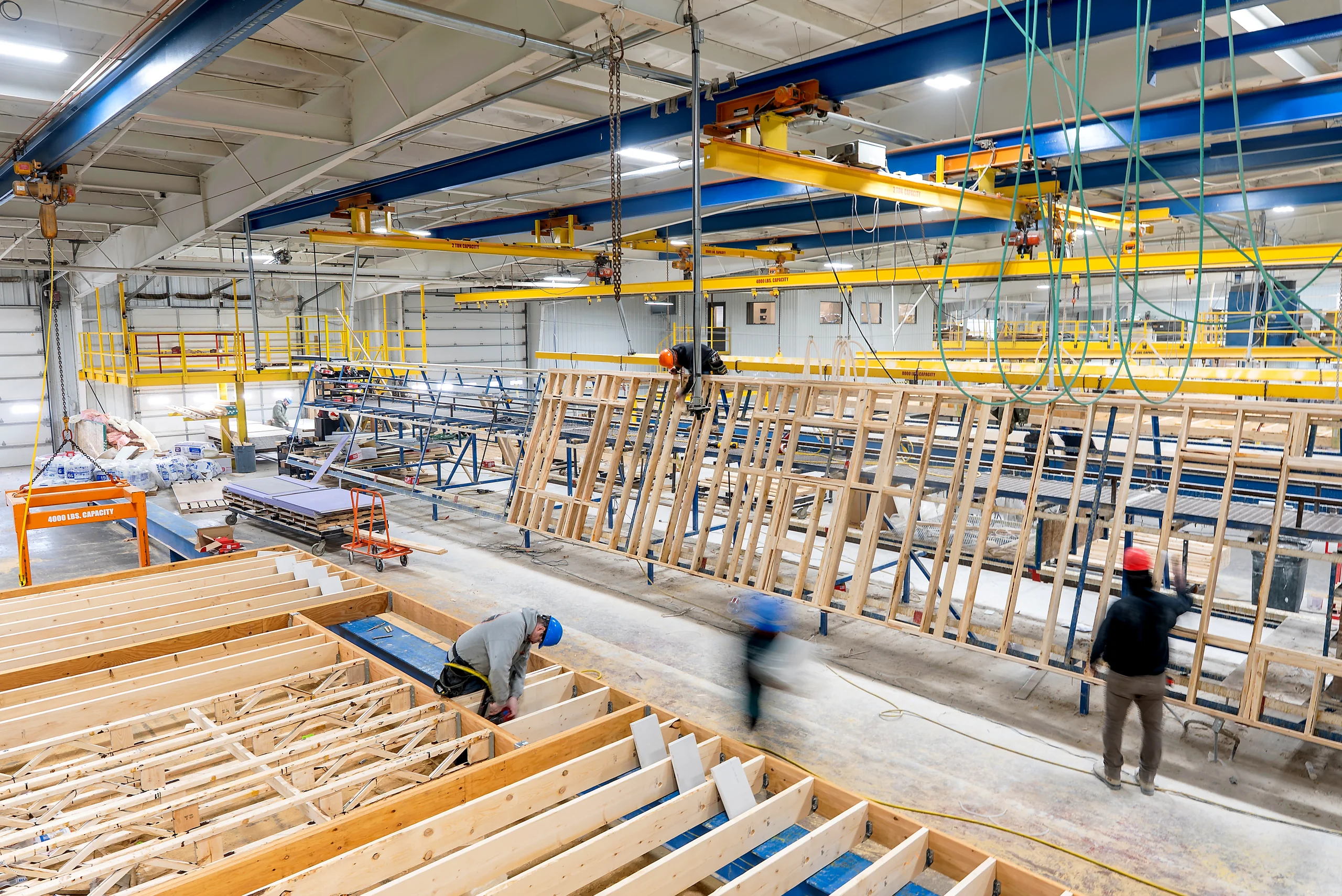 A prefabrication plant floor with modules moving down the line under an overhead crane