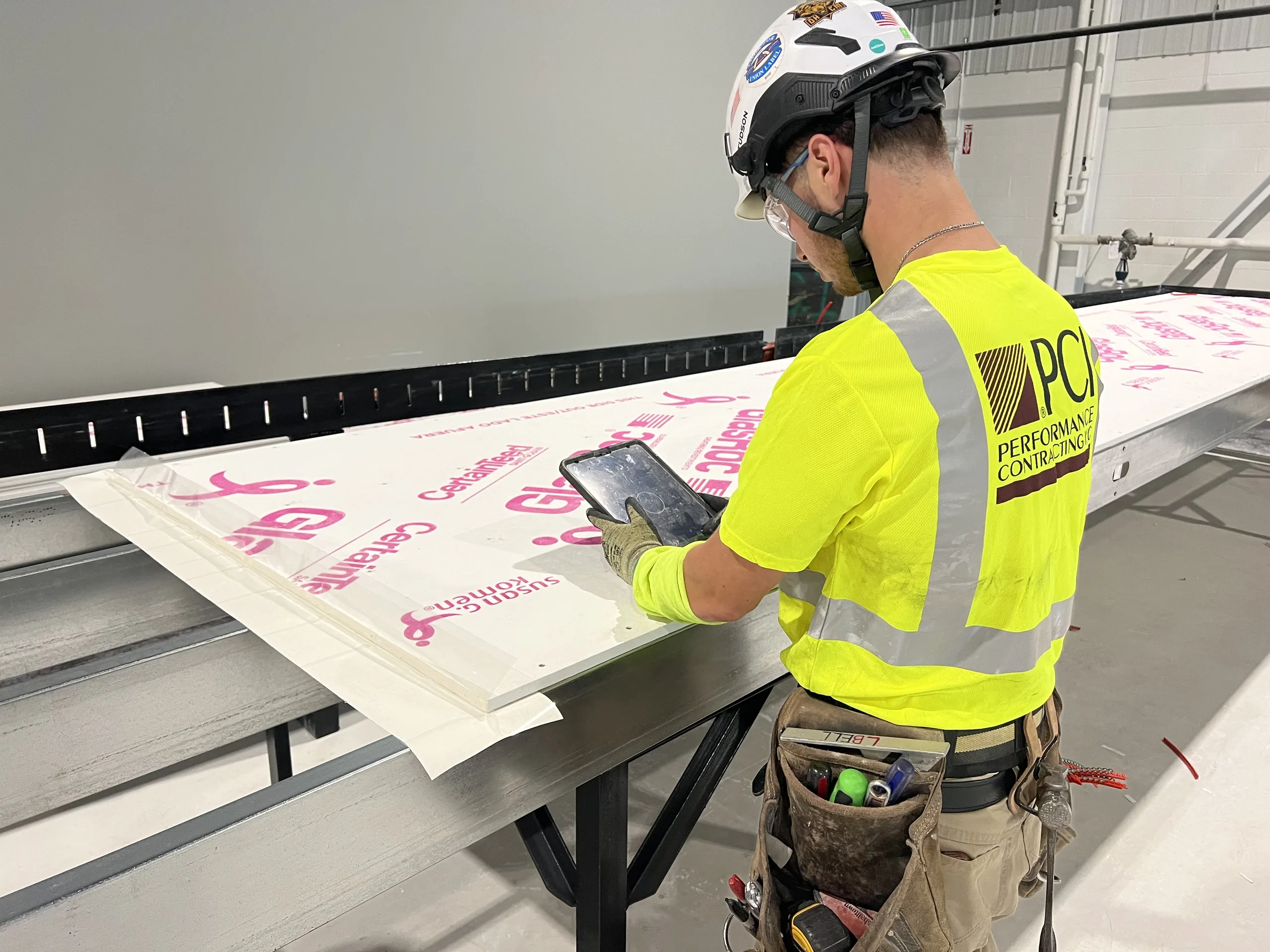 A Performance Contracting fabricator recording work on a tablet at the wall-panel table