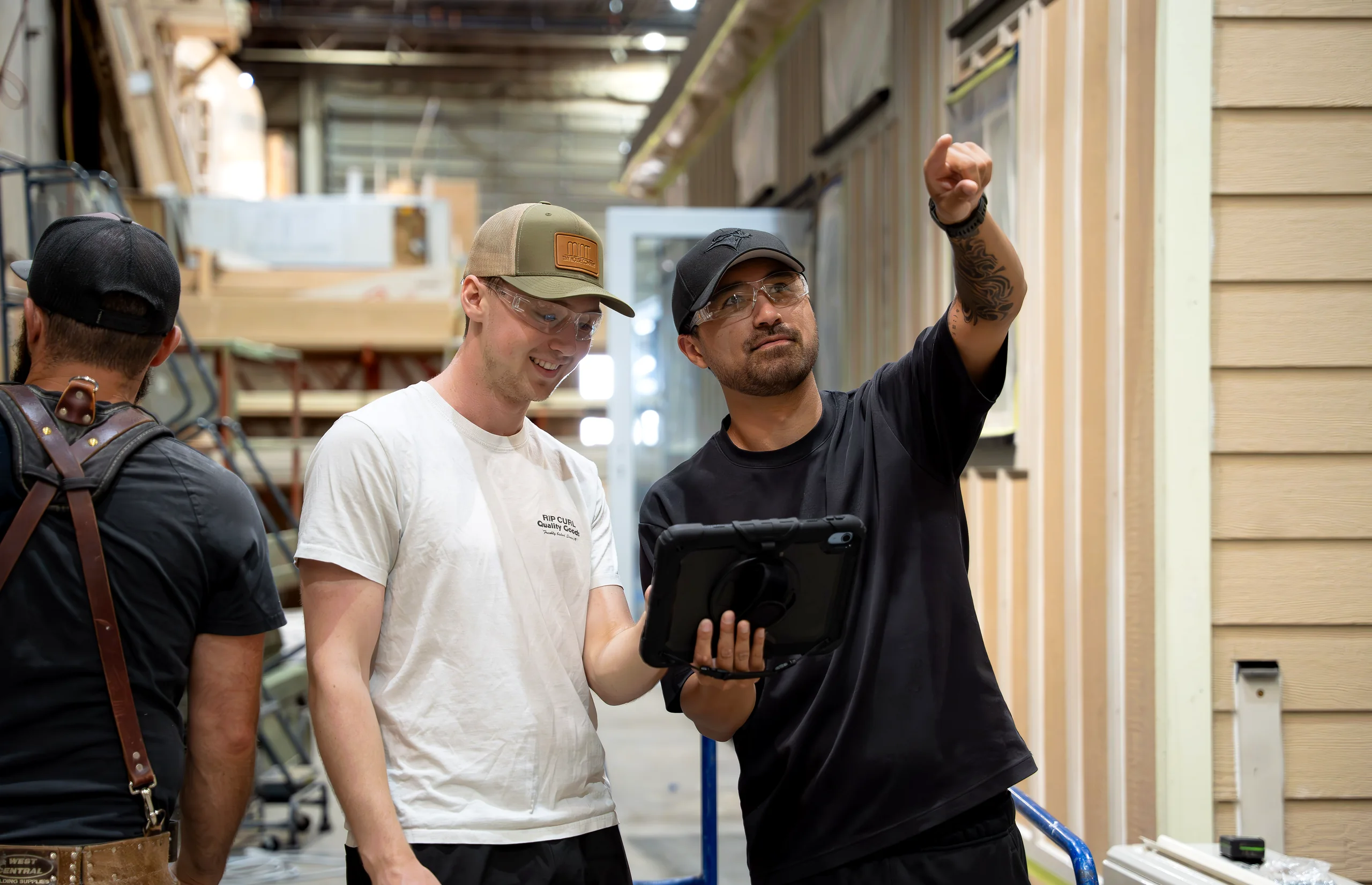 Three production workers on a factory floor, one holding a tablet