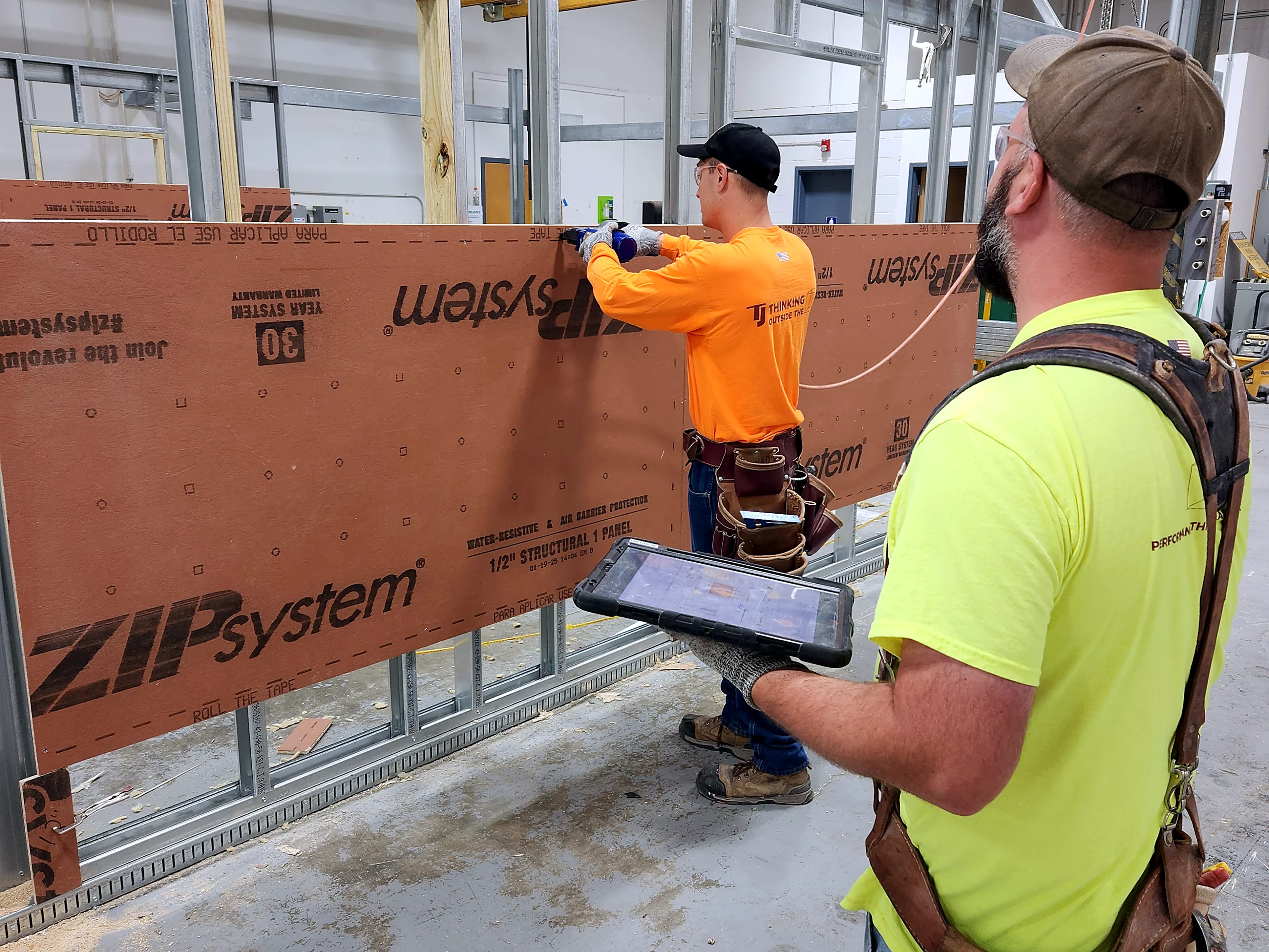Two TJ McCartney carpenters building a sheathed wall panel, one working from a tablet